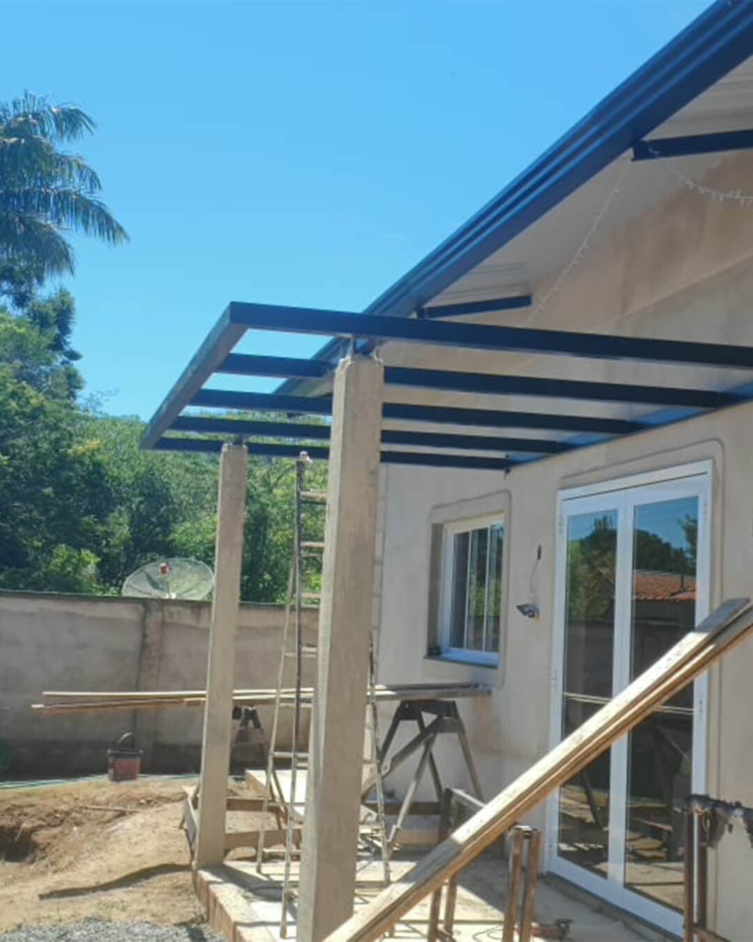 Estrutura metálica de cobertura em construção anexa à casa, com vigas escuras sobre pilares de concreto