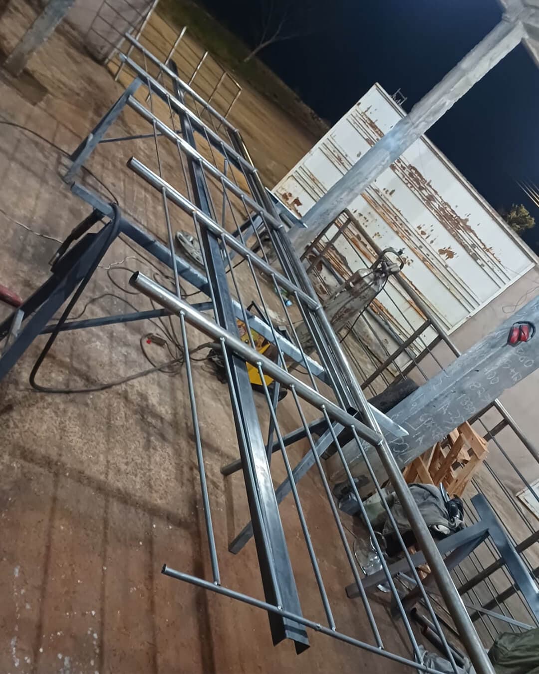 Grades e estruturas metálicas em fabricação com tubos de aço em oficina de serralheria à noite