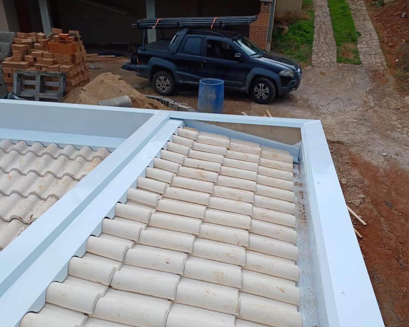 Estrutura de calhas e rufos brancos instalada em telhado de telhas cerâmicas em obra residencial