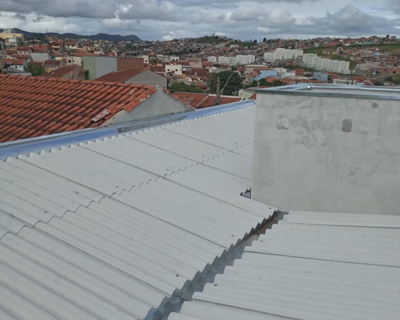 Telhado de telhas metálicas onduladas com rufos instalados junto à platibanda, com vista da cidade ao fundo