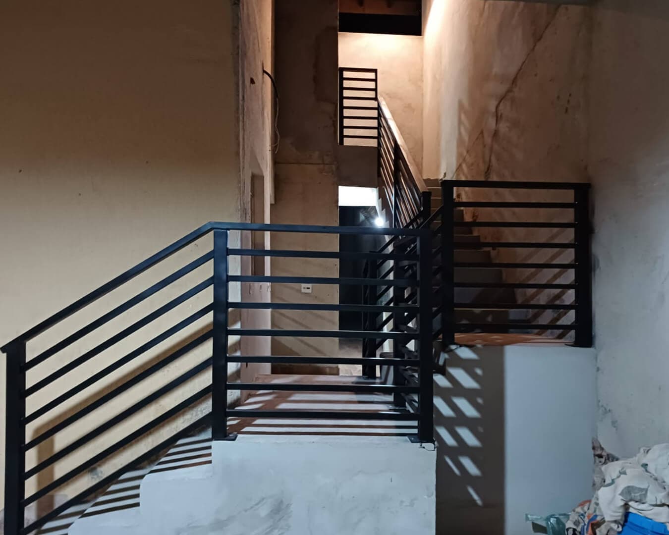 Guarda-corpo e corrimão metálicos pretos com barras horizontais instalados em escada interna de obra