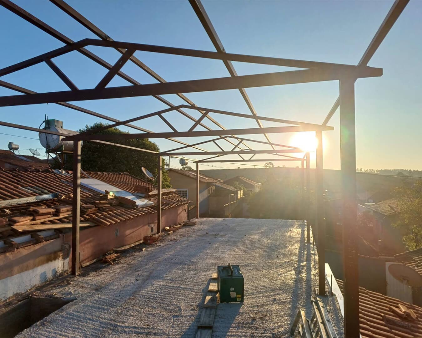 Estrutura metálica de telhado em montagem sobre laje, com treliças de aço ao pôr do sol